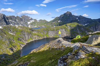 Mountaineer standing on a rock with green camping tent, mountain landscape with lake Tennesvatnet,