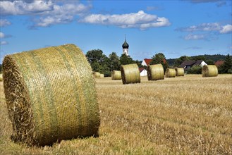 Straw bales on a harvested grain field, in the background the village church with onion tower,