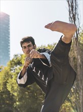 Handsome martial arts fighter practicing kicks outdoors while looking at camera