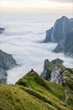 Two hikers enjoying the view over the Säntis mountains into the valley of Meglisalp at sunrise,