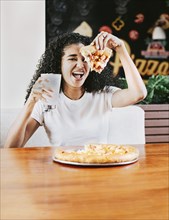 Happy afro hair woman showing slice of pizza in a restaurant. Smiling afro woman enjoying a pizza