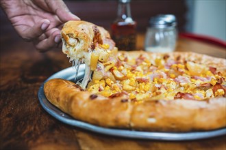 Hand taking a slice of ham and sweetcorn pizza. Homemade ham pizza with cheese and sweet corn