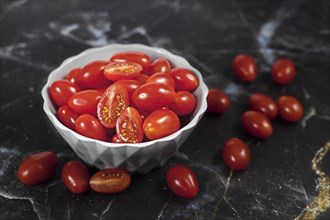 Ripe small red Roma cocktail tomatoes in white bowl on dark background