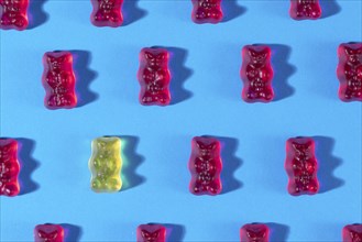 Red gummy bears and a yellow one in rows, on a blue background