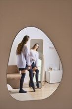 Reflection of woman dressing in front of mirror at home