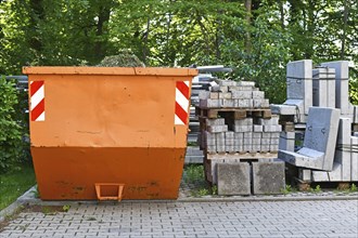 Orange industrial transportable dumpster container and cobble stones on palette at construction