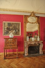 Red drawing room with chest of drawers, painting, wall mirror, parquet floor and fireplace,