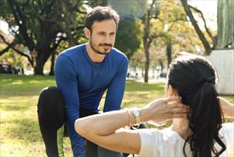 Male coach helping young woman exercising in park