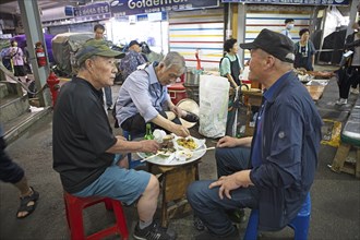 Old men sitting on plastic stools and eating at Gwangjang Market, traditional street market in