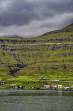 Little village on the foot of a the cliffs in Estuyroy, Faroe islands, Denmark, Europe