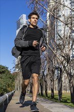 Motivated handsome man jogging by green public park