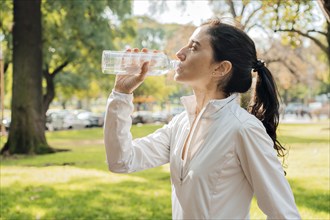 Middle age woman in profile drinking water after training in the park