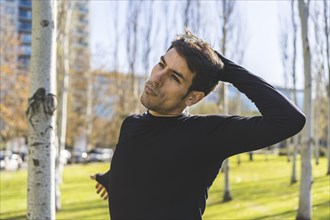 Sporty handsome man stretching neck and head after jogging in city public park