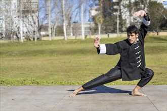 Young athletic martial arts fighter practicing kicks in a public park wearing classic kung fu