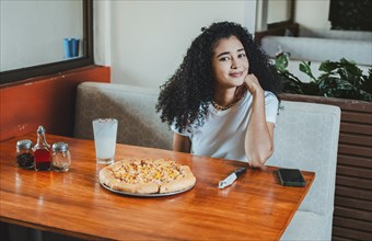 Beautiful afro hair girl in a pizzeria restaurant. Lifestyle of afro-haired girl sitting in a