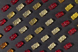 Different coloured gummy bears in rows, on a dark background