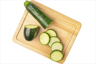 Courgettes (Cucurbita pepo), sliced, on wooden board, on white