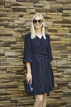 Medium closeup portrait of smiling woman in dotted black dress accessorised with sunglasses and