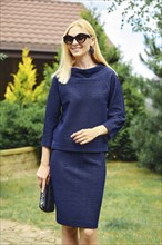 Smiling woman in knitted blue blouse and skirt on pathway of the garden