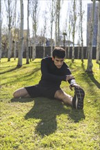 Sporty handsome man stretching legs after working out in city public park