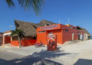 Thatched palapa roofed buildings and bright orange exterior of Los Pampanos seaside restaurant,