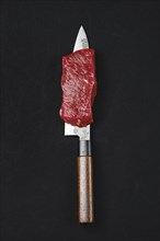 Piece of raw strip steak on the blade of knife