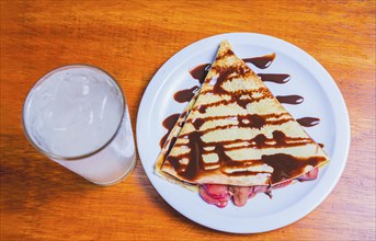 Crepe with chocolate cream and strawberry with drink on the table. Sweet strawberry crepe with