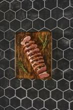 Overhead view of a seared duck breast cut on slices on wooden chopping board