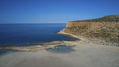 Coastline with sandy beach, clear blue sky and rocky cliffs at the edge of the blue sea,