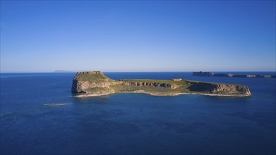 Drone shot, Small, secluded island with rocky coastline surrounded by the wide, blue sea under a