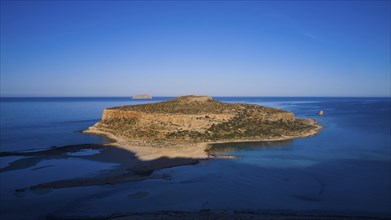 Drone image, aerial view of a large island with a steep rocky coast, surrounded by clear blue sea,