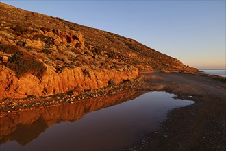 A road next to a reflecting puddle of water at sunrise lighting in a rocky landscape, Gramvoussa