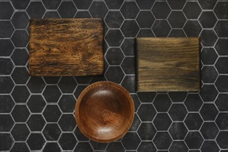 Top view of empty round wooden bowl and cutting boards on a black hexagonal tiled background