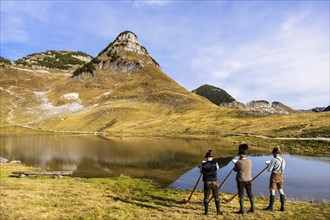 Three men play the alphorn at Lake Augstsee on Mount Loser. The Austrian alphorn trio Klangholz.