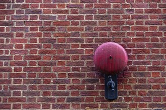 Close-up of a red brick wall with a red alarm bell