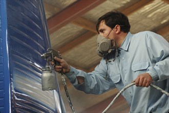 Tradesman sprays blue topcoat on the tail of a Dornier 228 aircraft