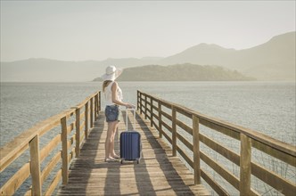 Great vacation concept. Young woman holding her suitcase, waiting for the boat on the dock