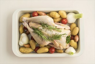 Roast chicken prepared for roasting with young garlic, shallots, parsley, cherry tomatoes, potatoes