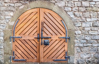 Ancient wooden door with metal hinged and latch, on a weathered stone wall