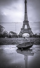 Monochrome image with Eiffel Tower on a rainy day and an upside down umbrella in a puddle in