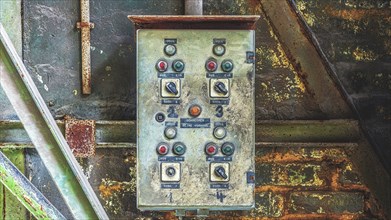 A rusty old switch box with several buttons and switches in a wall-mounted industrial environment,