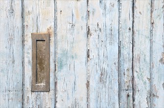 Close up of an old wooden door with blue faded paint and a rusty closed old metal brass letterbox