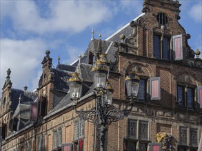 Historic brick building with ornate windows and decorative lanterns under a cloudy sky, nijmegen,