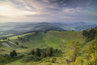 An impressive panorama of mountains with rocky peaks and dense forests under a cloudy sunset,