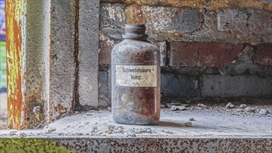 An obsolete sulphuric acid bottle stands on a dusty windowsill in an industrial setting,