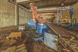 Abandoned factory building with a large orange-coloured robot arm amidst machines and equipment,