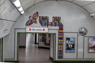 Interior view of an underground station with colourful wall art and No Entry sign, London, United