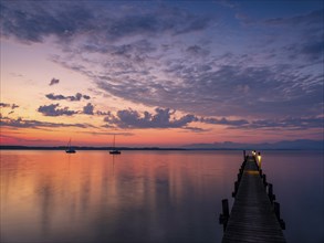 Sailing boats and jetty on Lake Chiemsee at dawn, with the Chiemgau Alps in the background,