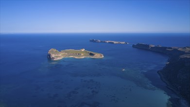 Drone shot, aerial view of an island with green area surrounded by blue sea and steep cliffs,