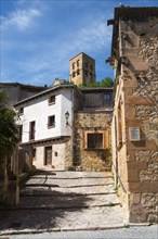 Narrow alleyway with cobblestones and historical buildings, in the background a bell tower, sunny